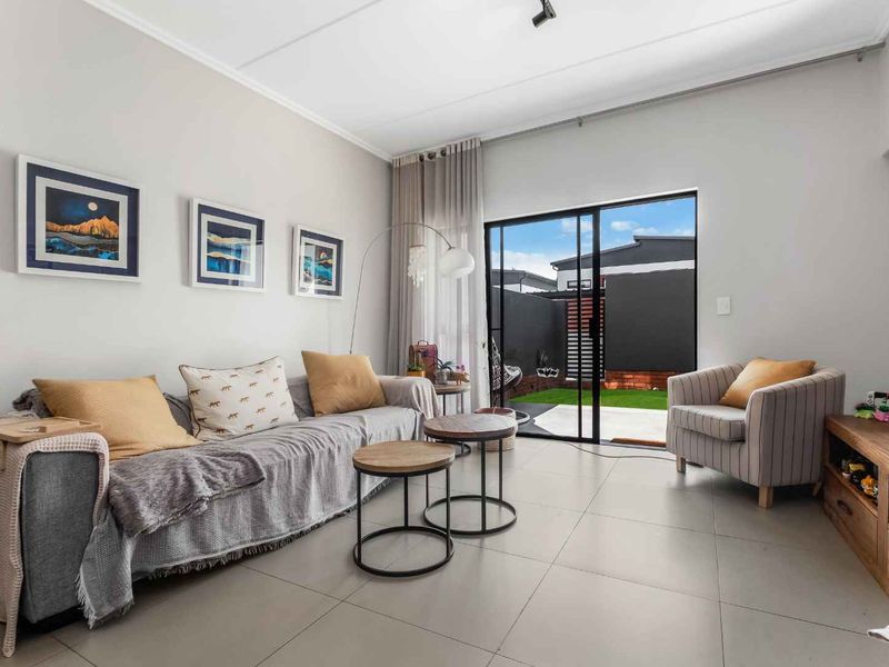 A bright living room featuring large format floor tiles and a sliding glass door providing direct access to the rear patio and garden area.