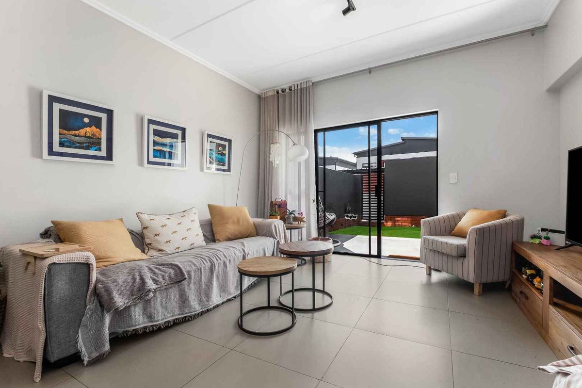 A bright living room featuring large format floor tiles and a sliding glass door providing direct access to the rear patio and garden area.