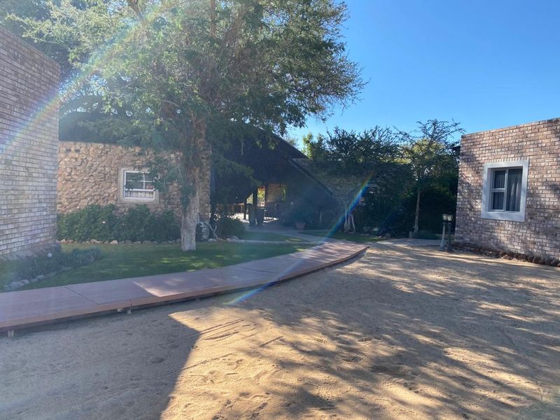A view of the rear exterior featuring brick and stone buildings connected by a timber walkway, set within a landscaped garden area.