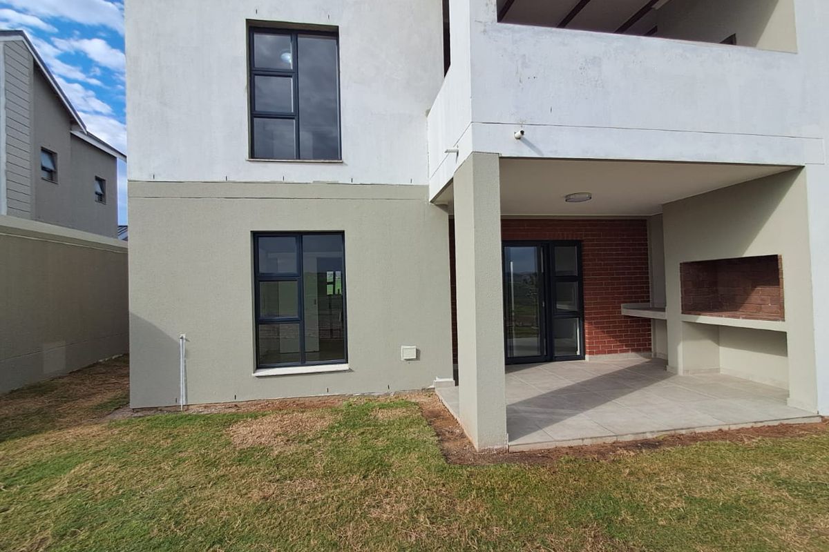 Rear view of the apartment featuring a covered patio with a built-in brick braai, tiled flooring, and modern aluminium window frames.