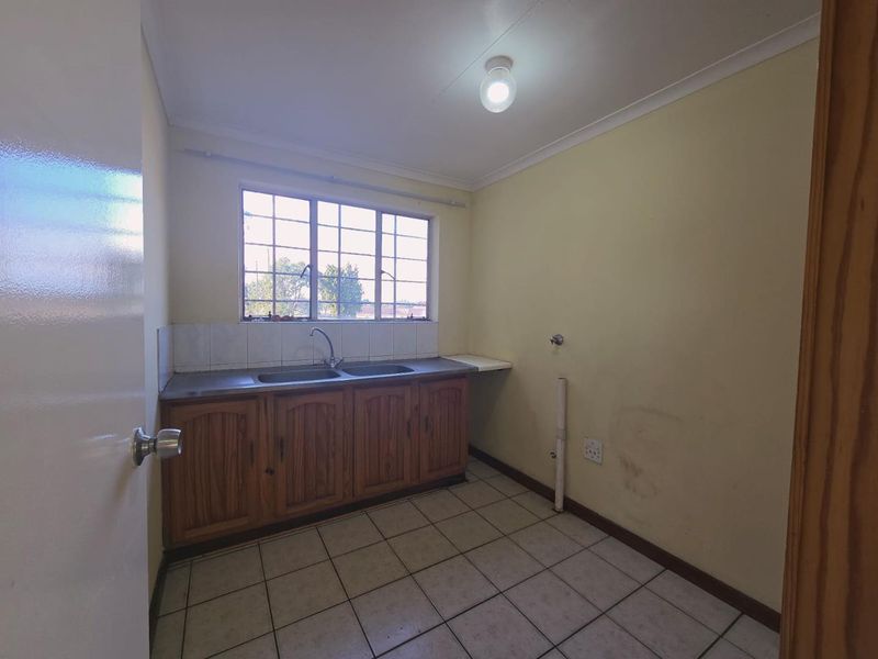 A functional laundry room featuring tiled flooring, built-in wooden cabinetry with a double sink, and plumbing connections for appliances.