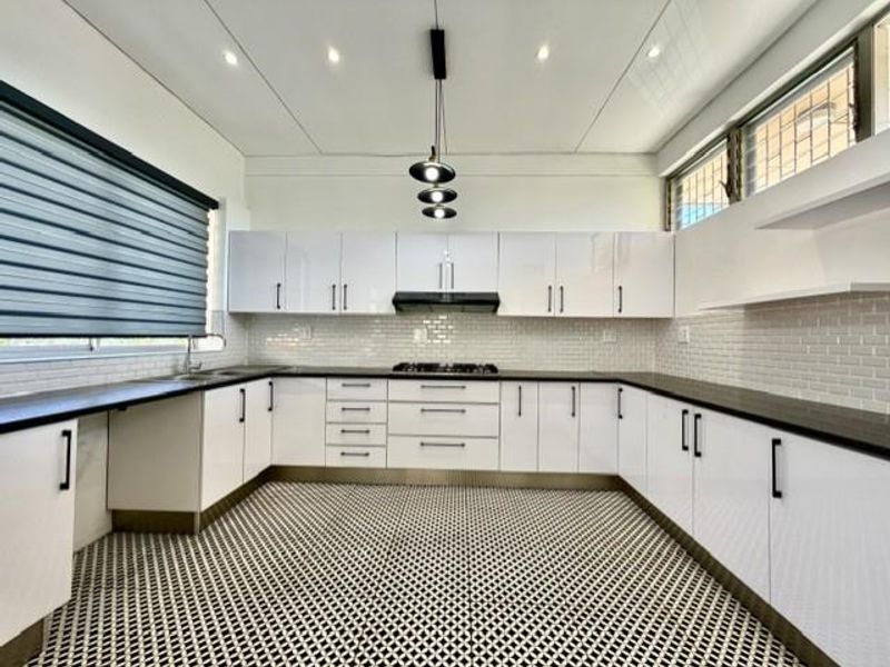 Modern, well-lit kitchen featuring white high-gloss cabinetry, a gas hob with extractor fan, subway tile backsplash, and patterned floor tiles.