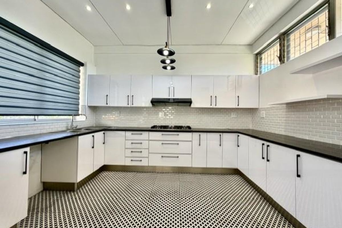 Modern, well-lit kitchen featuring white high-gloss cabinetry, a gas hob with extractor fan, subway tile backsplash, and patterned floor tiles.