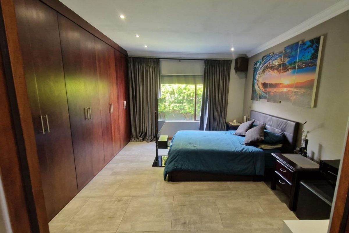 Spacious bedroom featuring large built-in wooden wardrobes, tiled flooring, recessed ceiling lighting, and a window with curtain treatments.