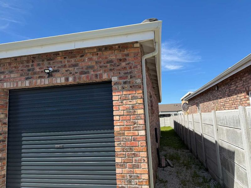 Side view of the property showing the face brick garage exterior, roller door, guttering system, and precast concrete boundary wall.