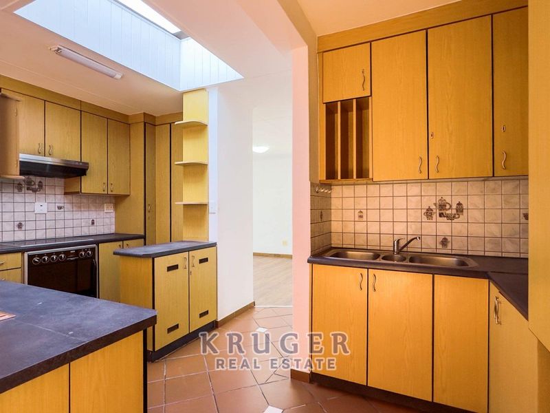 A functional kitchen featuring light wood-tone cabinetry, dark countertops, a double sink, built-in oven, and a skylight providing natural overhead lighting.