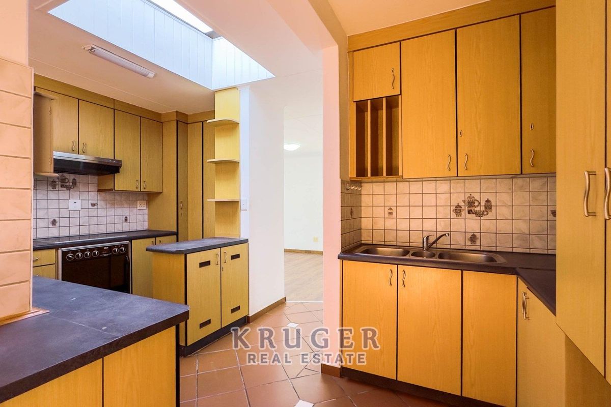 A functional kitchen featuring light wood-tone cabinetry, dark countertops, a double sink, built-in oven, and a skylight providing natural overhead lighting.