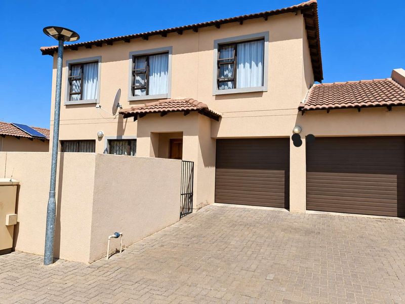 Front elevation of a double-story townhouse featuring a paved driveway, double garage, and neutral exterior finish under a tiled roof.