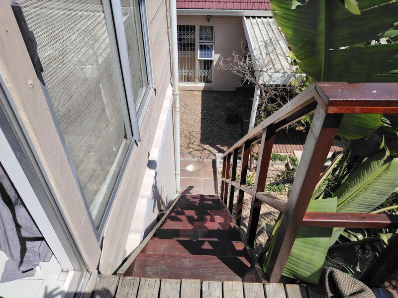 An elevated view looking down a timber staircase leading to a rear garden area with paved pathways and security-fitted access points.