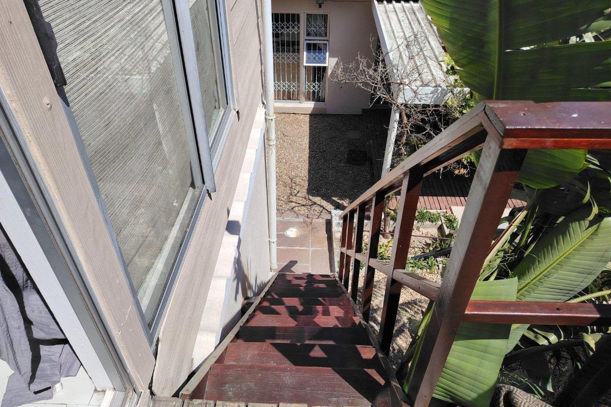 An elevated view looking down a timber staircase leading to a rear garden area with paved pathways and security-fitted access points.