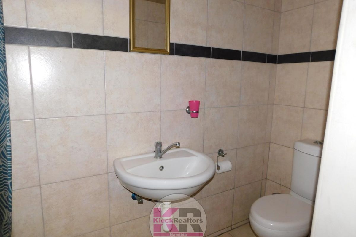 A functional bathroom featuring a wall-mounted basin, a standard toilet, and neutral wall tiling with a decorative black accent border.