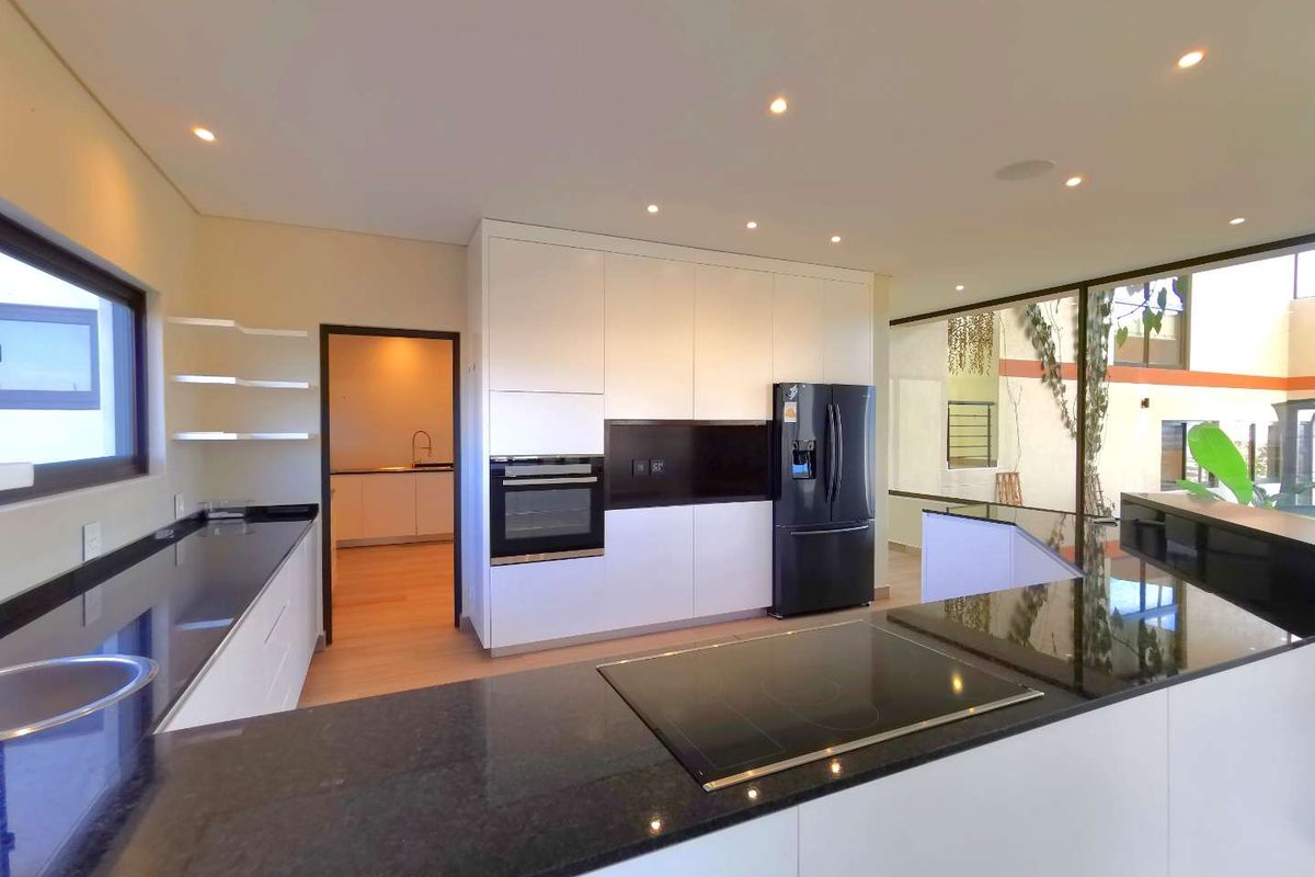 Modern kitchen featuring sleek white cabinetry, black granite countertops, integrated oven, and a built-in induction hob, with an adjacent scullery area.