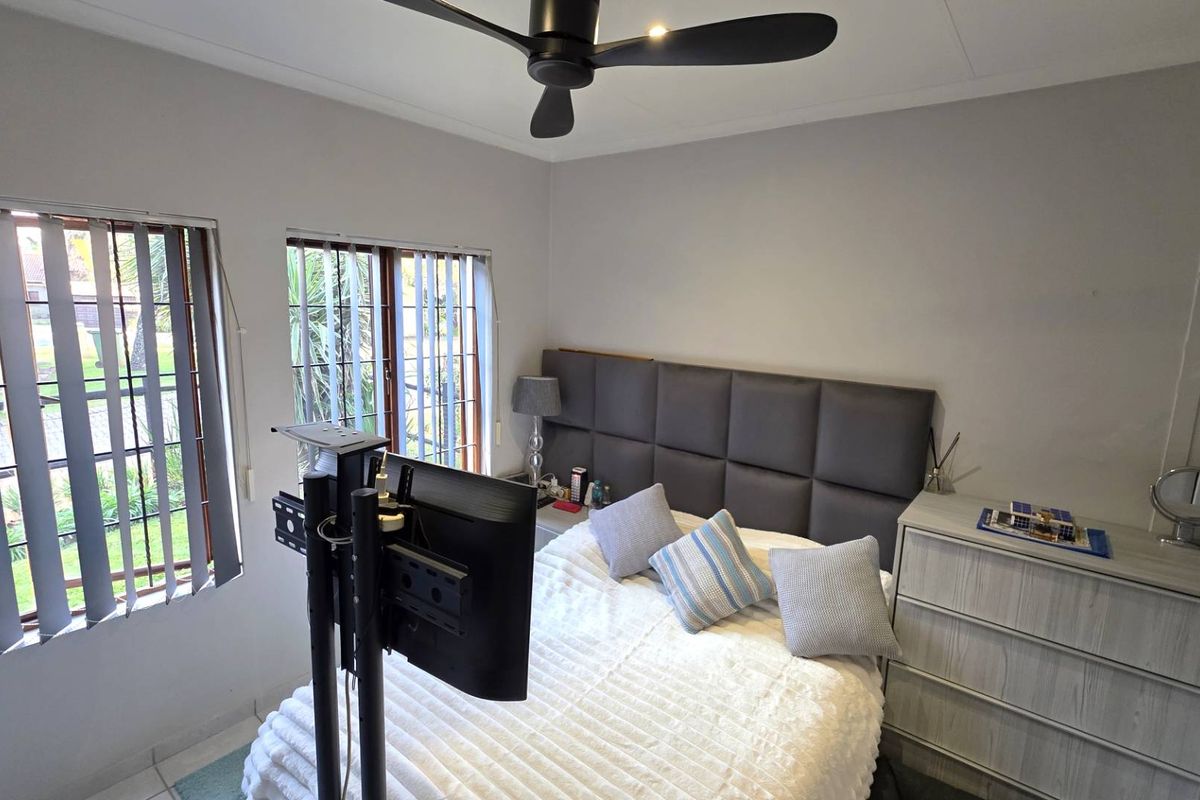 A bedroom featuring a ceiling fan, tiled flooring, and large windows with vertical blinds, providing natural light and a view of the exterior.