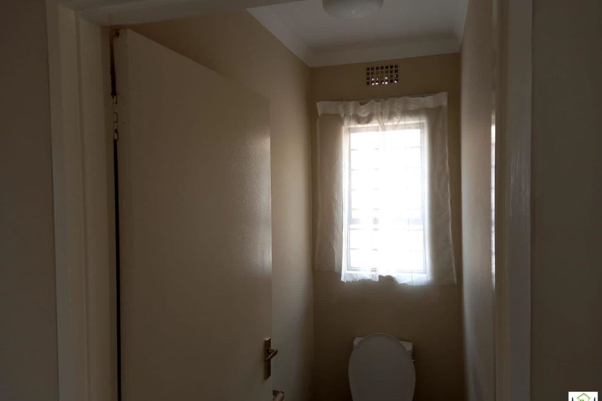 A compact, functional bathroom featuring a standard toilet and a window with security bars, providing natural light and ventilation.