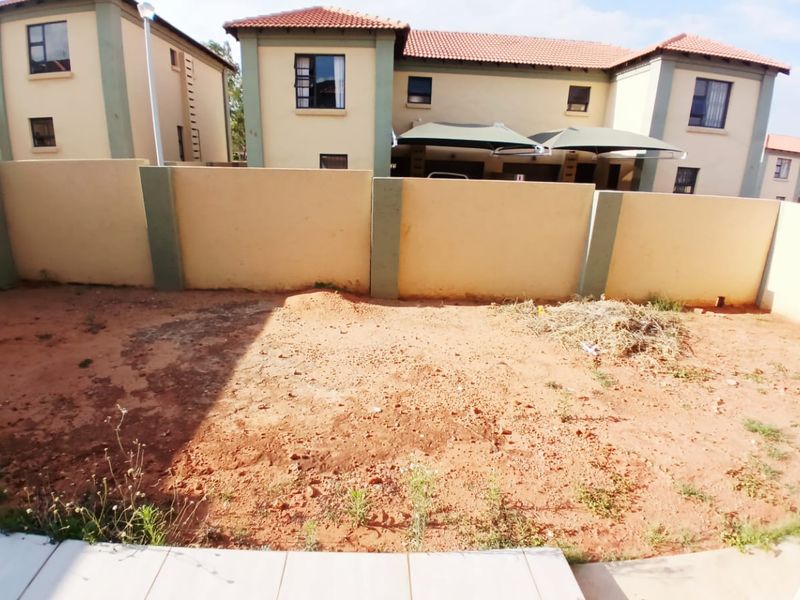 A rear exterior view of a residential property featuring a tiled patio area and an unlandscaped garden space enclosed by a perimeter wall.