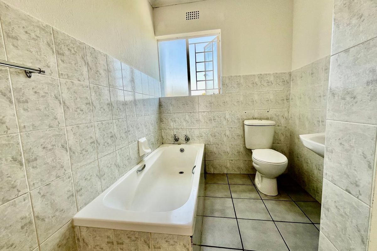 A functional bathroom featuring a built-in bathtub, standard toilet, and wall-mounted basin with tiled walls and flooring.