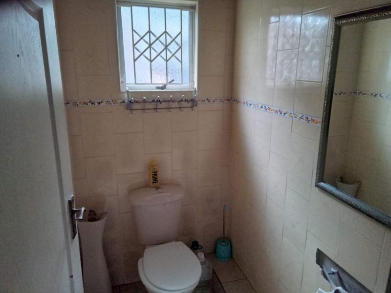 A compact bathroom featuring tiled walls, a standard toilet, and a wall-mounted mirror, requiring cosmetic updates to improve its dated appearance.