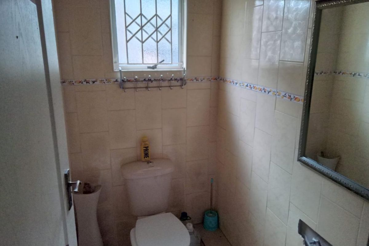 A compact bathroom featuring tiled walls, a standard toilet, and a wall-mounted mirror, requiring cosmetic updates to improve its dated appearance.