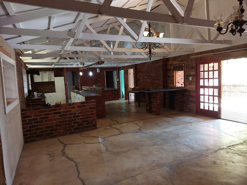 Spacious open-plan living area featuring exposed timber roof trusses, rustic brick walls, and polished concrete flooring with direct access to the outdoors.