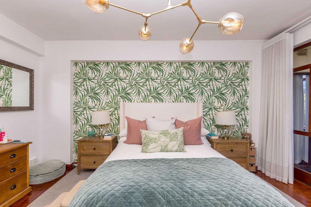 A well-maintained bedroom featuring a decorative botanical wallpaper feature wall, hardwood flooring, and a contemporary pendant light fixture.