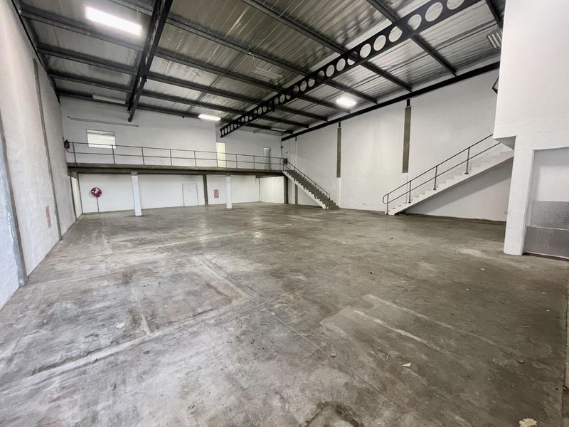 Spacious industrial warehouse unit featuring high ceilings with exposed steel trusses, a mezzanine level, concrete flooring, and internal staircase access.