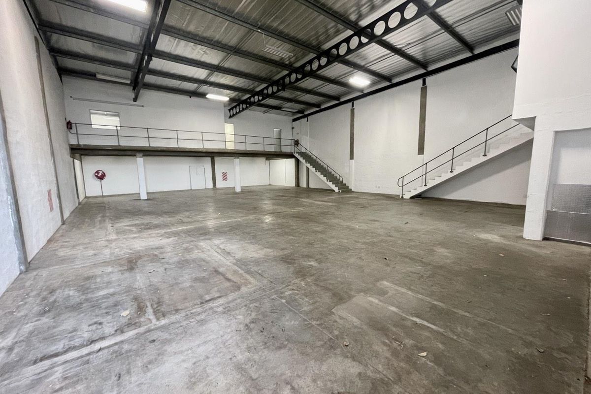 Spacious industrial warehouse unit featuring high ceilings with exposed steel trusses, a mezzanine level, concrete flooring, and internal staircase access.