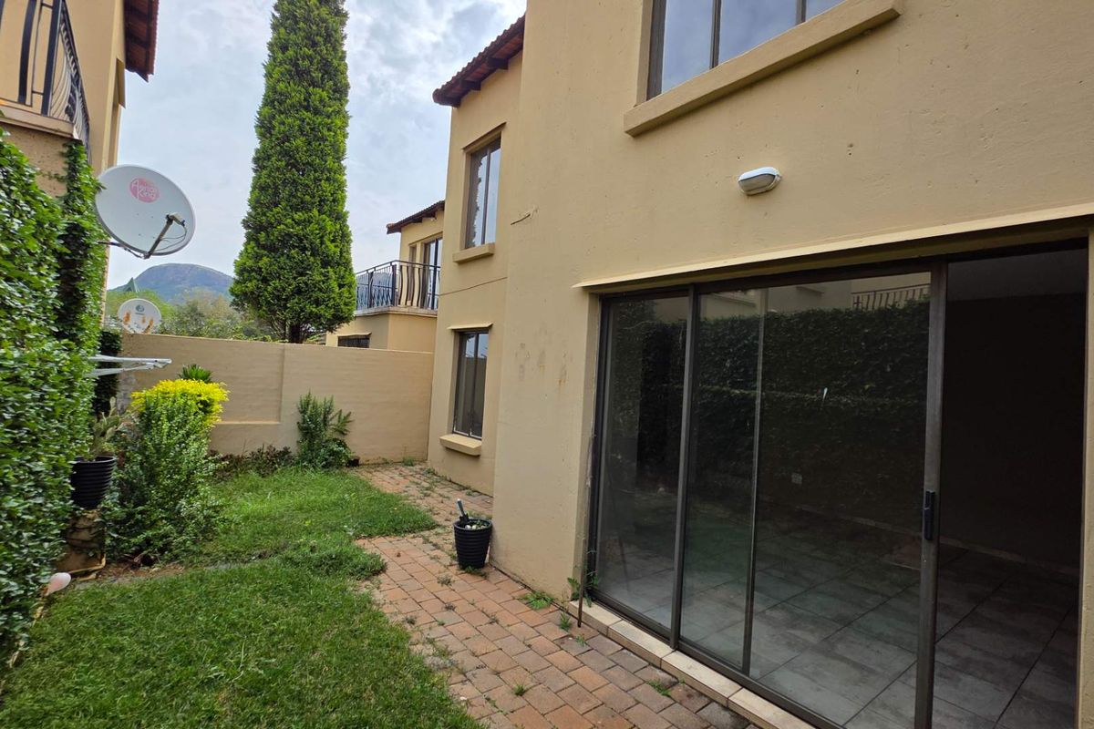 Rear view of the townhouse featuring a paved patio area, sliding glass doors, and a small private garden space.