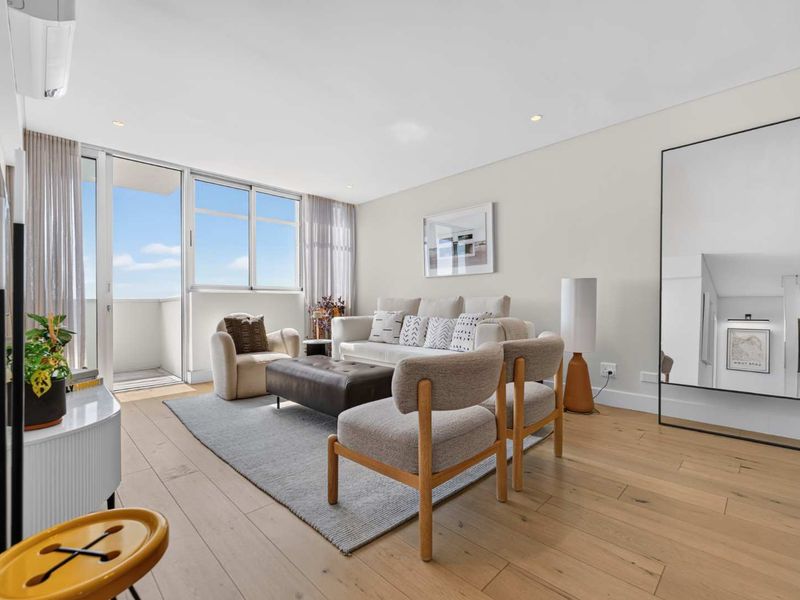 Bright and modern living room featuring light timber flooring, recessed lighting, and large sliding glass doors leading to a private balcony.