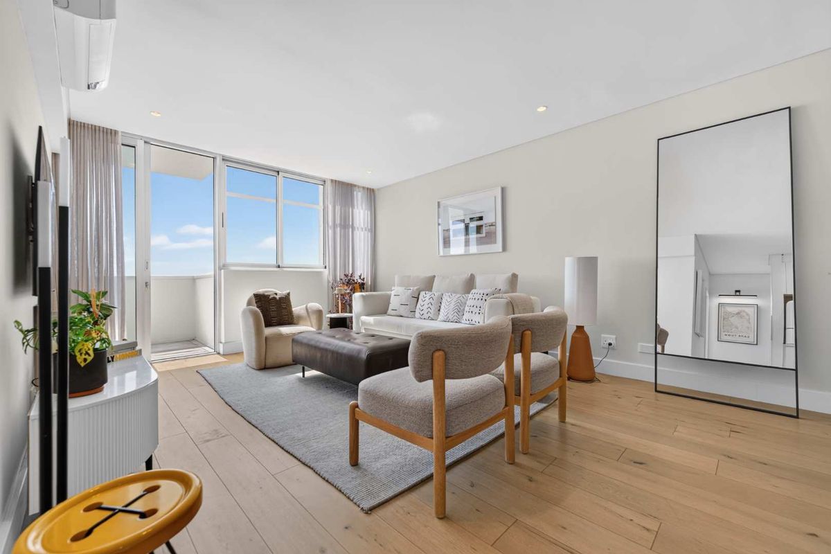 Bright and modern living room featuring light timber flooring, recessed lighting, and large sliding glass doors leading to a private balcony.