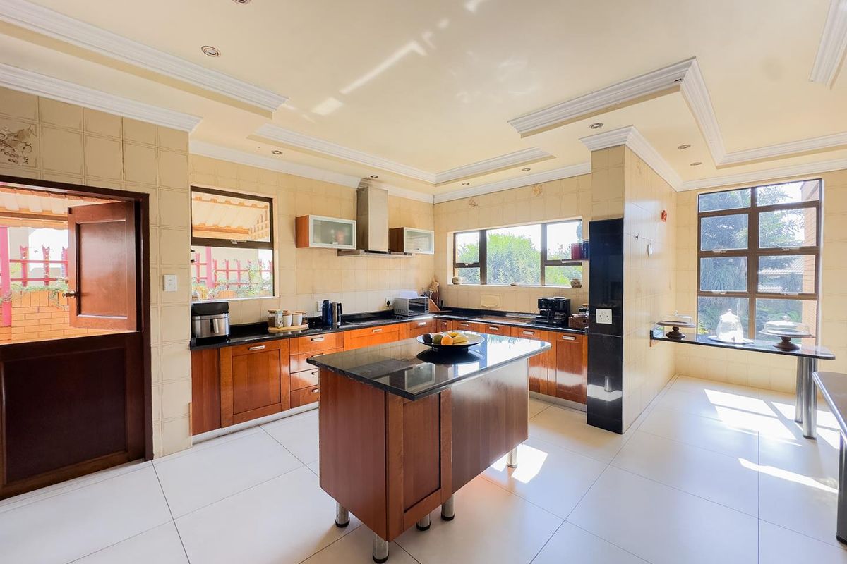 Spacious kitchen featuring wooden cabinetry, a central island with a dark stone countertop, integrated extractor fan, and large windows providing ample natural light.