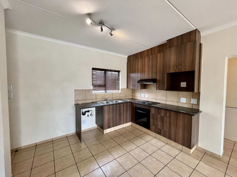 A functional kitchen featuring dark wood cabinetry, granite-look countertops, built-in oven and hob, and tiled flooring throughout.