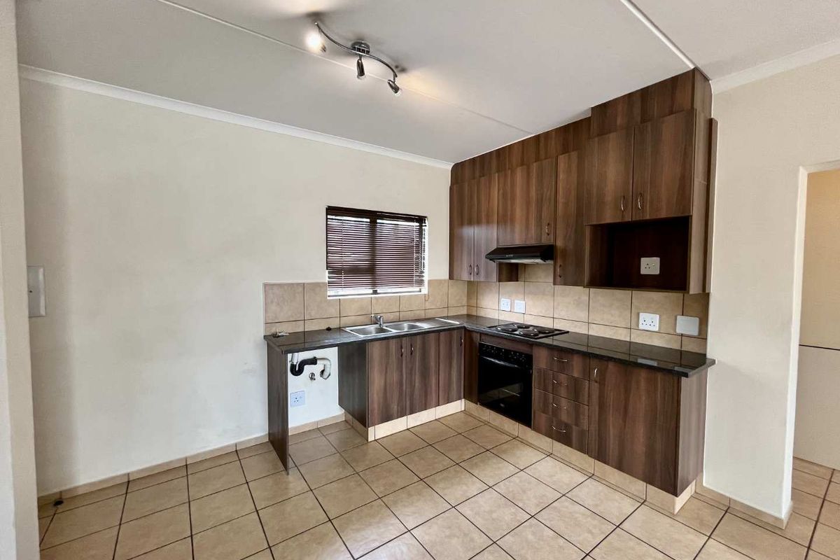 A functional kitchen featuring dark wood cabinetry, granite-look countertops, built-in oven and hob, and tiled flooring throughout.
