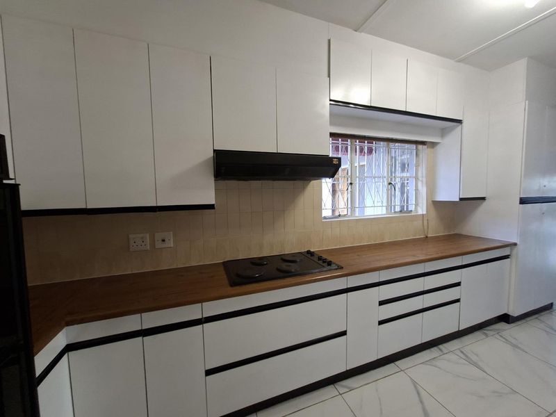 Modern kitchen featuring white cabinetry, wooden countertops, an integrated electric hob with extractor fan, and tiled flooring.