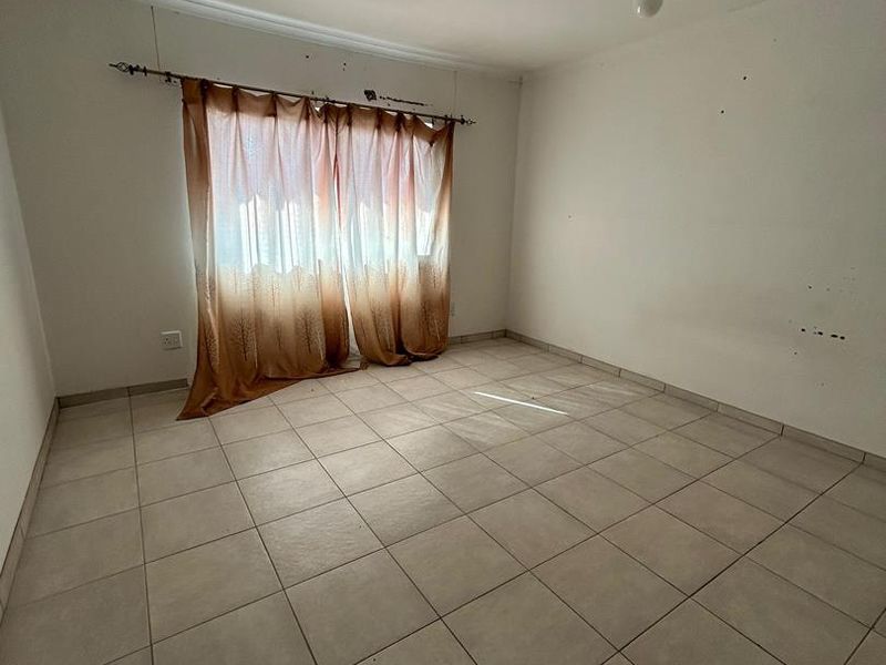 An empty bedroom featuring neutral ceramic floor tiles and basic ceiling lighting, ready for a fresh coat of paint and new interior design.