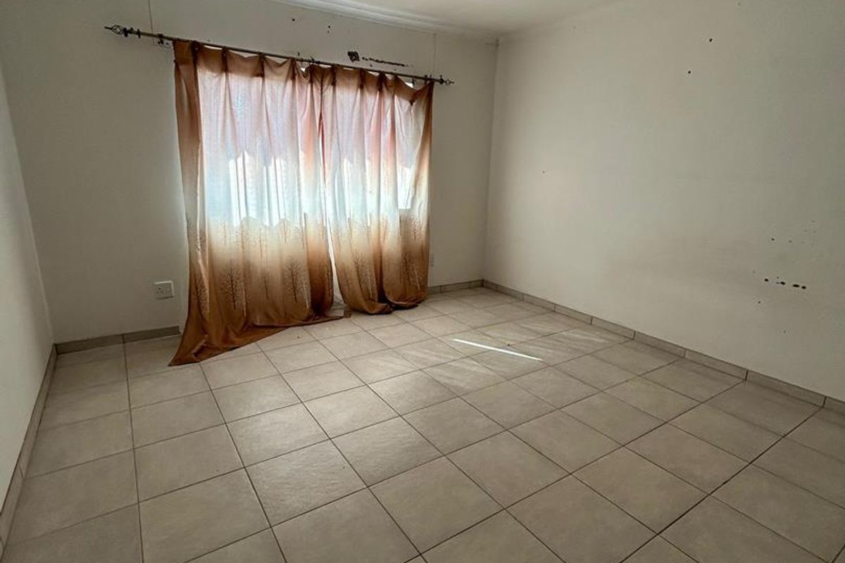An empty bedroom featuring neutral ceramic floor tiles and basic ceiling lighting, ready for a fresh coat of paint and new interior design.