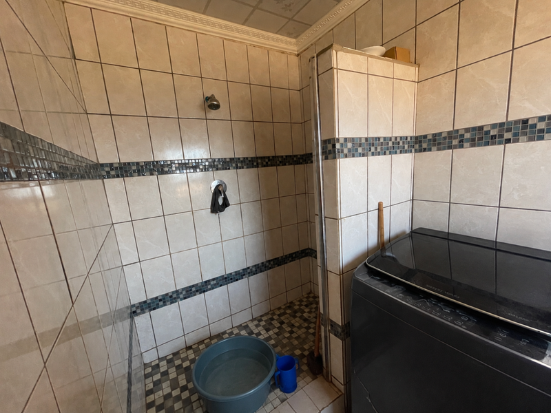 A functional bathroom featuring full-height wall tiling with a decorative mosaic border and a built-in shower area.