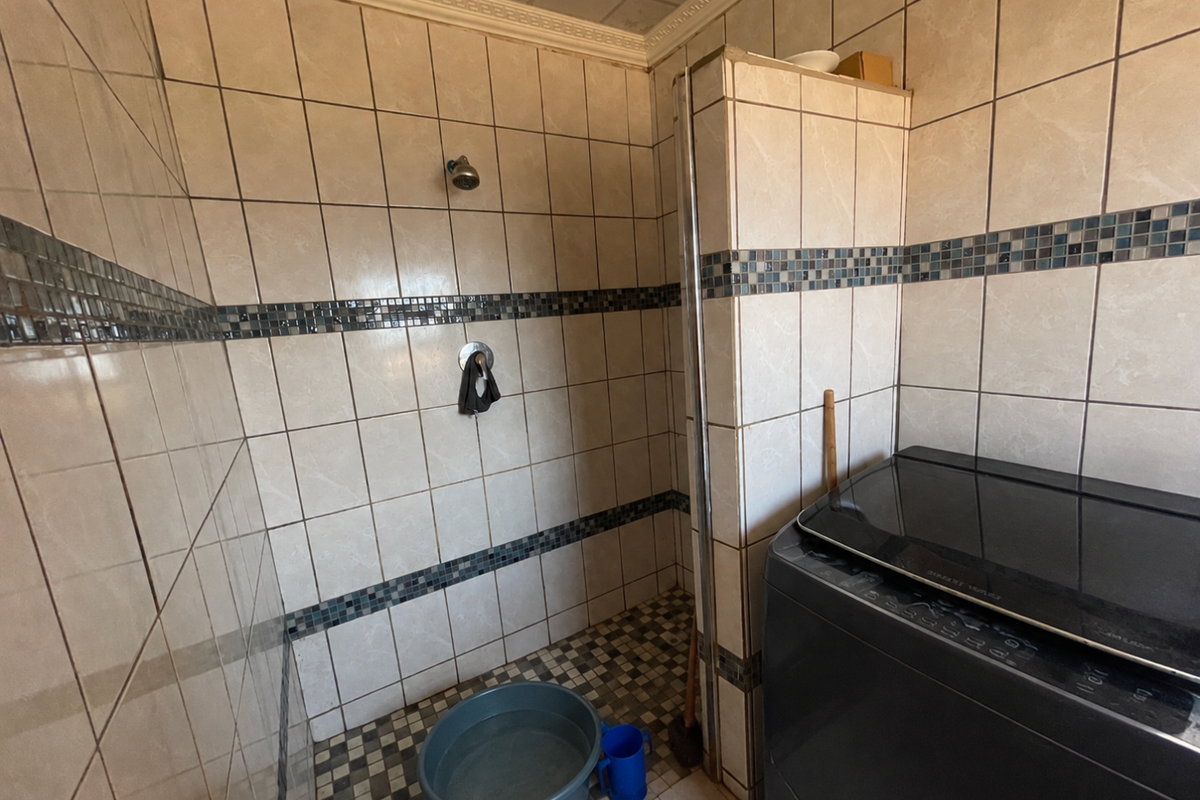 A functional bathroom featuring full-height wall tiling with a decorative mosaic border and a built-in shower area.