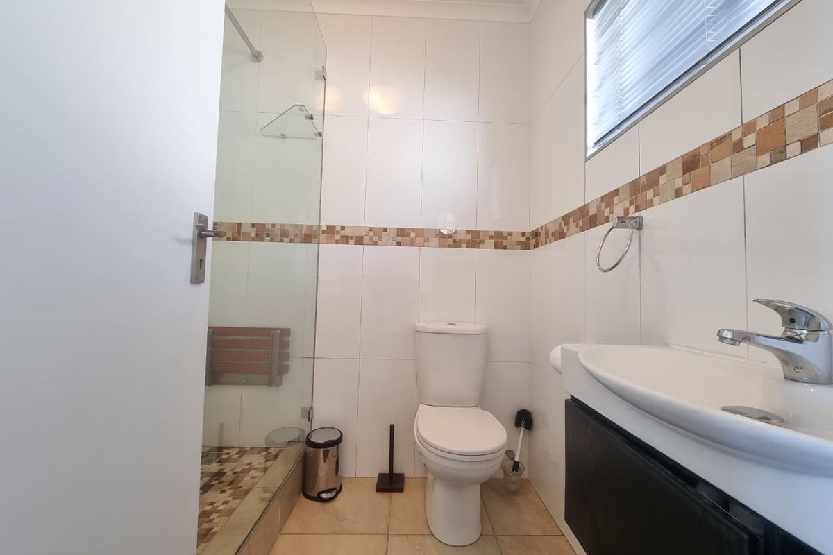 A compact bathroom featuring a glass-enclosed shower, a wall-mounted vanity with a basin, and a standard toilet with tiled walls and flooring.