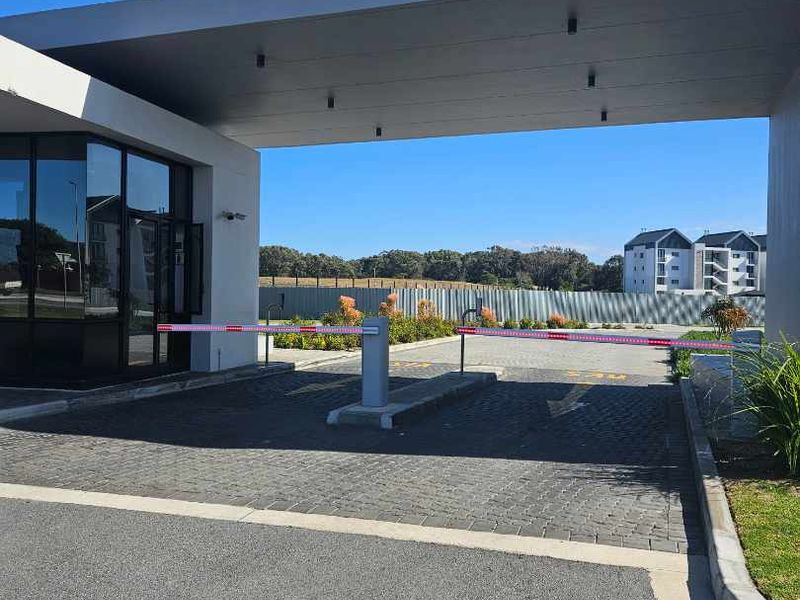 Modern secure apartment complex entrance featuring a paved driveway, security boom gate, and a contemporary covered guard house canopy.