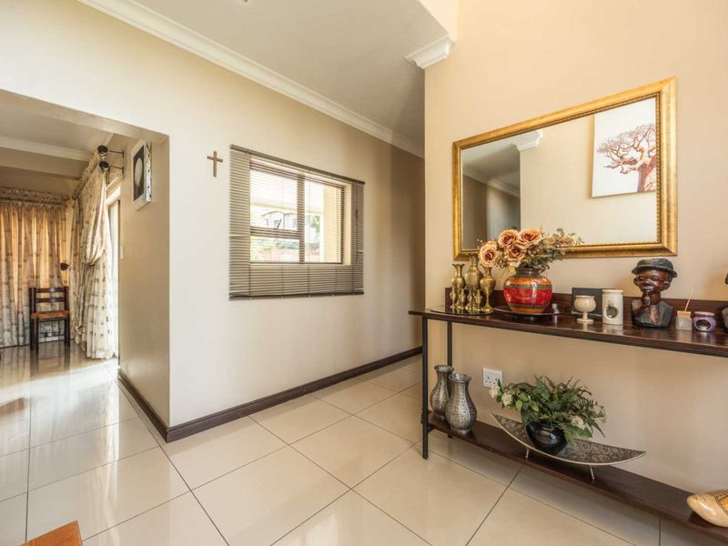 A bright and well-maintained hallway featuring neutral tiled flooring, decorative cornicing, and a window with a fitted venetian blind.