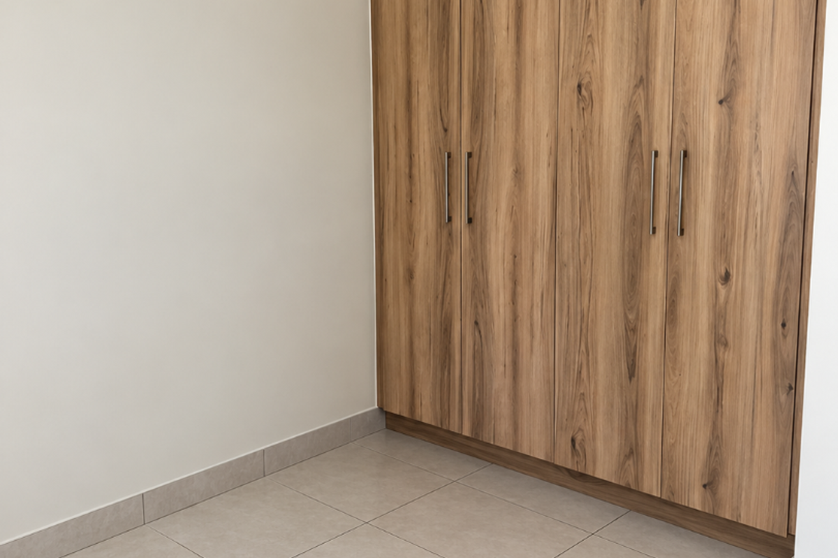 A clean, empty bedroom featuring modern wood-finish built-in cupboards and neutral tiled flooring, offering a versatile space ready for personalization.