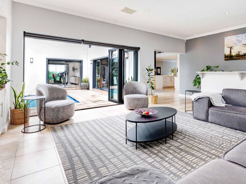 Spacious open-plan living area featuring large bi-fold doors that open onto a patio and pool area, with neutral finishes and recessed lighting.