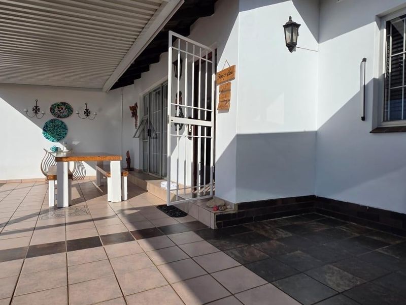 A covered outdoor patio area featuring tiled flooring, a security gate, and external lighting, providing a functional space for outdoor living.
