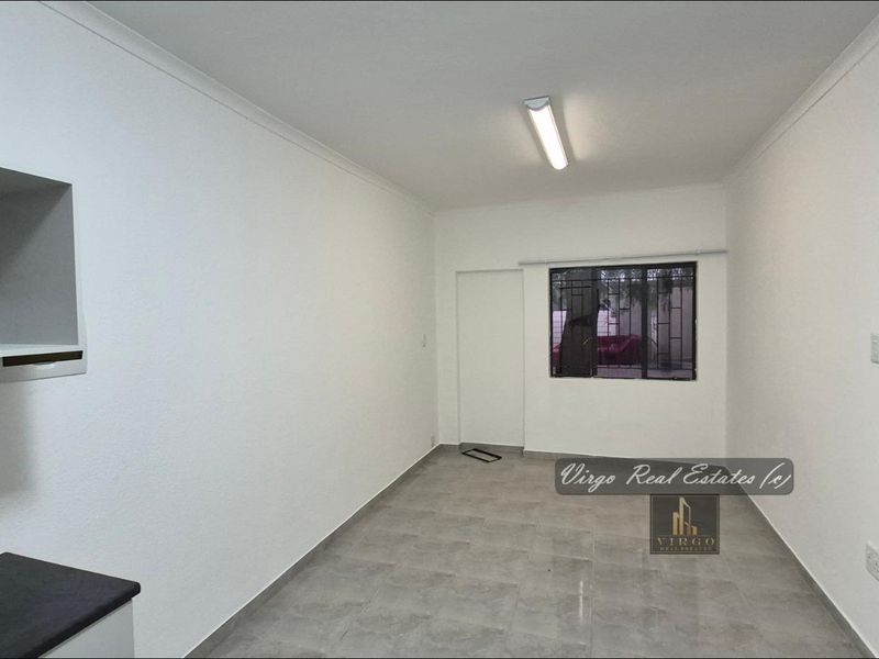 A clean, empty kitchen space featuring tiled flooring, built-in shelving, and a window with security bars.