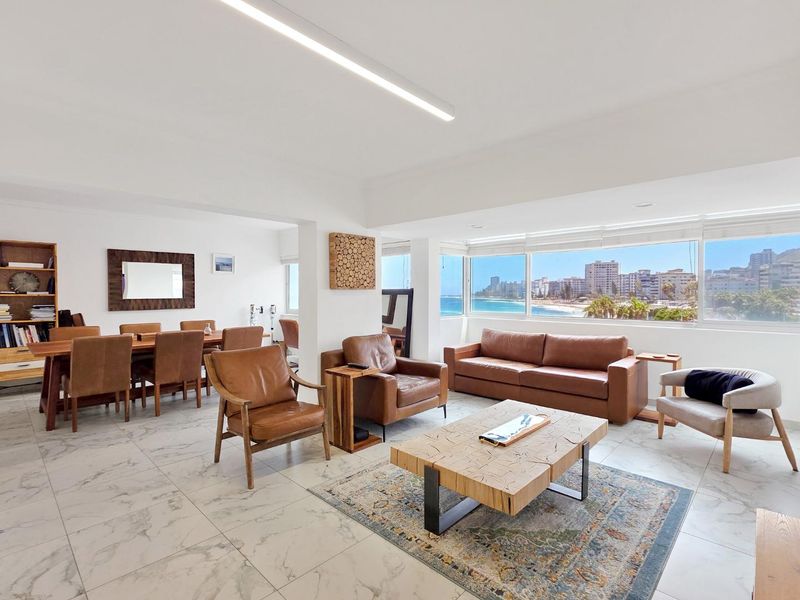 Spacious open-plan living and dining area featuring large panoramic windows with coastal views and modern marble-look floor tiles.
