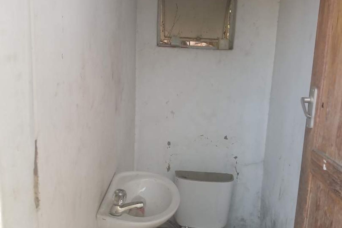 A small, basic bathroom featuring a wall-mounted basin and a toilet, currently in a state of significant disrepair and requiring extensive renovation.