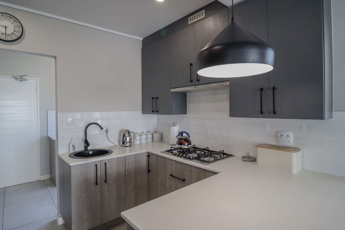 Modern kitchen featuring dark grey cabinetry, stone countertops, subway tile backsplash, and a gas cooktop with integrated extractor fan.