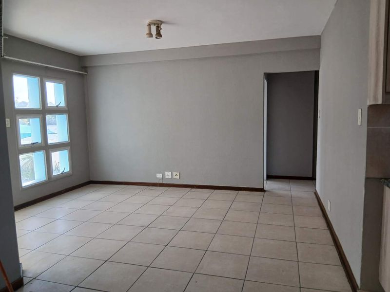 An empty, open-plan living area featuring neutral grey walls, tiled flooring, and a multi-pane window providing natural light.