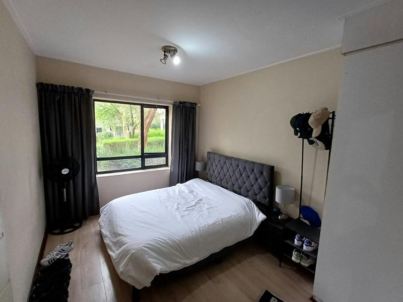 A functional bedroom featuring laminate flooring, a large window providing natural light, and a ceiling-mounted spotlight fixture.