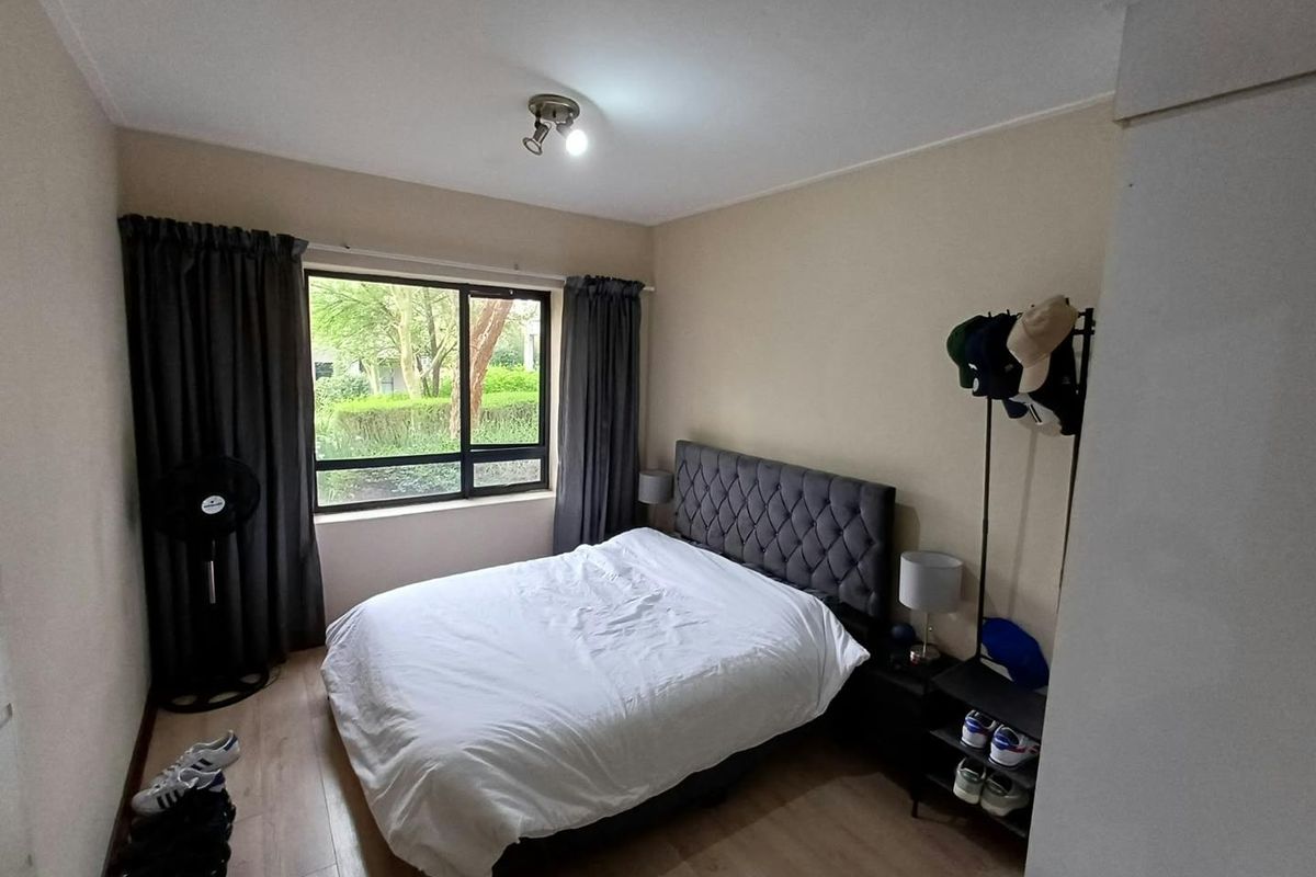 A functional bedroom featuring laminate flooring, a large window providing natural light, and a ceiling-mounted spotlight fixture.